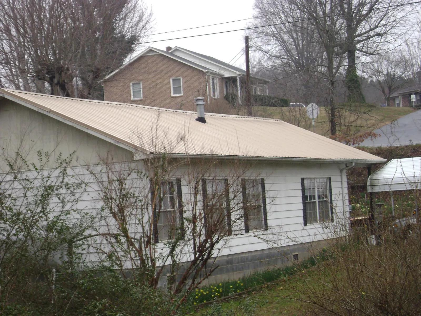 Tan metal roof on a white sided house set into a hillside — Commercial Roofing by Roofing Brothers in Taunton